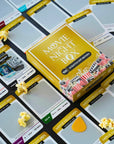 Movie Night Box from Date Night Brands featuring 100 scratch-off movie cards spread out on a table, showcasing genres like horror, sci-fi, and comedy, with a QR code for movie details, surrounded by popcorn for a cinematic experience.